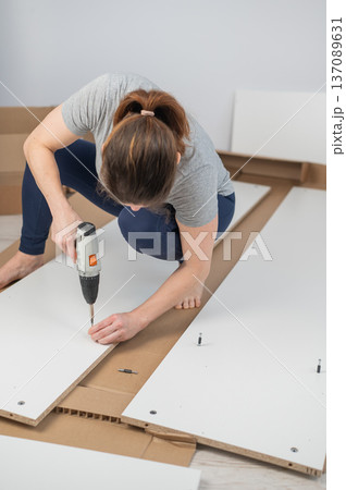A Caucasian woman uses a screwdriver to tighten a screw while assembling a cabinet. 137089631