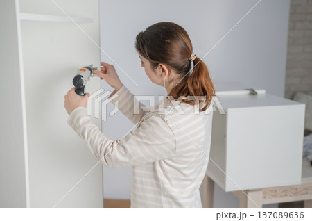 A Caucasian woman uses a screwdriver to tighten a screw while assembling a cabinet. 137089636