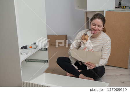 A Caucasian woman assembles furniture with her cute dog. A Caucasian woman assembles furniture with her cute dog. 137089639