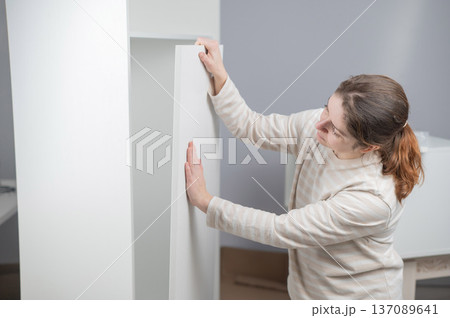 A Caucasian woman assembles a wardrobe. 137089641