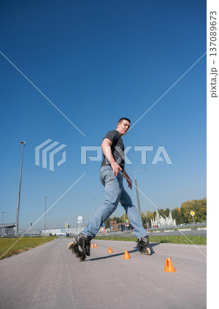 A Caucasian man rollerblades around the slalom course. A Caucasian man rollerblades around the slalom course. 137089673