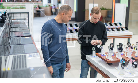 Two Caucasian men choose smartwatches in a tech store. 137089675