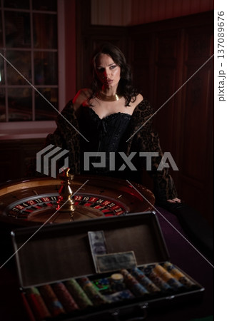 A beautiful brunette in a black dress at the casino roulette wheel.  137089676