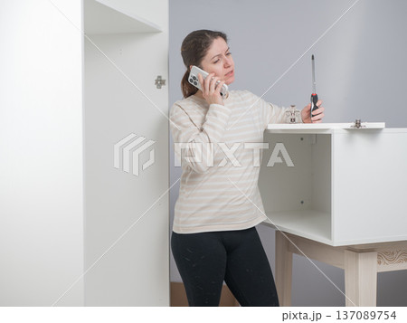 A Caucasian woman talks on the phone while assembling furniture. A Caucasian woman talks on the phone while assembling furniture. 137089754