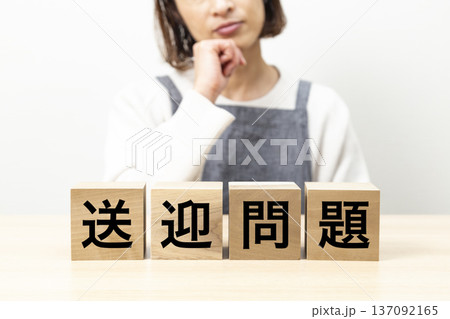 「送迎問題」と書かれたブロックとエプロン姿で悩む女性 「送迎問題」と書かれたブロックとエプロン姿で悩む女性 137092165