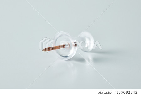 A single transparent map tack with a metal needle point, isolated on a light surface A single transparent map tack with a metal needle point, isolated on a light surface 137092342