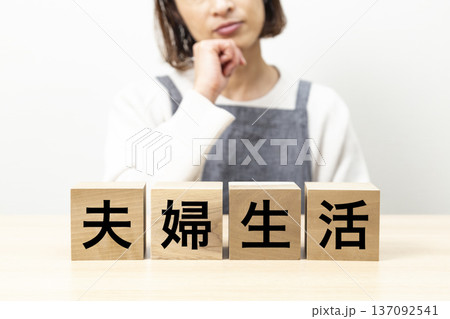 「夫婦生活」と書かれたブロックとエプロン姿で悩む女性 「夫婦生活」と書かれたブロックとエプロン姿で悩む女性 137092541