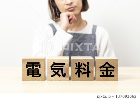 「電気料金」と書かれたブロックとエプロン姿で悩む女性 「電気料金」と書かれたブロックとエプロン姿で悩む女性 137092662