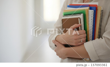 Student Clutching Notebooks In Bright Corridor, Closeup Of Hands And Stack Of Folders, Soft Hallway Light And Blurred Background, Posture Conveys Readiness For Tutorial Or Office Hours, 137093361