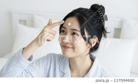 寝室で額に保湿クリームを乗せて微笑む日本人女性 137094680