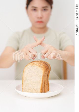 Unhappy woman showing Rejecting gesture and refusing to eat bread. concept of gluten intolerance, gluten sensitivity, carb loading concerns, or a disliking for unhealthy dietary habits 137096116