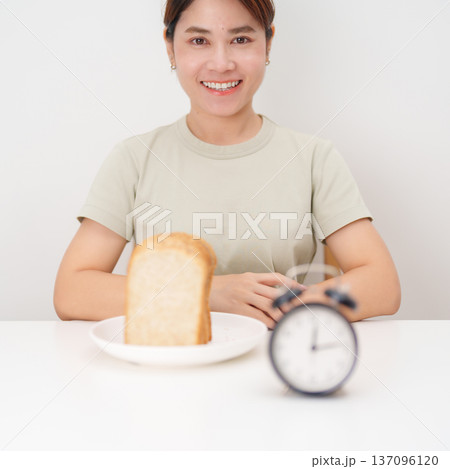 Happy smiling woman with whole wheat bread and alarm clock. concept of intermittent fasting, IF, meal timing, and choosing healthy carbohydrates for a balanced diet and weight loss management Happy smiling woman with whole wheat bread and alarm clock. concept of intermittent fasting, IF, meal timing, and choosing healthy carbohydrates for a balanced diet and weight loss management 137096120