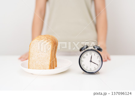 Happy smiling woman with whole wheat bread and alarm clock. concept of intermittent fasting, IF, meal timing, and choosing healthy carbohydrates for a balanced diet and weight loss management 137096124