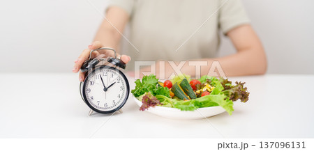 happy smiling woman with fresh organic vegetables plate and alarm clock. intermittent fasting, IF, meal time, nutrition, weight loss, clean eating, Healthy food eating, Wellness, dieting and lifestyle 137096131