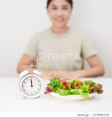 happy smiling woman with fresh organic vegetables plate and alarm clock. intermittent fasting, IF, meal time, nutrition, weight loss, clean eating, Healthy food eating, Wellness, dieting and lifestyle happy smiling woman with fresh organic vegetables plate and alarm clock. intermittent fasting, IF, meal time, nutrition, weight loss, clean eating, Healthy food eating, Wellness, dieting and lifestyle 137096138