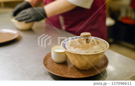 Preparing meal. Restaurant bowl. Chef in gloves serving food order with sauce on cafeteria kitchen table. Portion hot dish with lid. Preparing meal. Restaurant bowl. Chef in gloves serving food order with sauce on cafeteria kitchen table. Portion hot dish with lid. 137096611