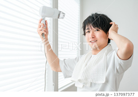 お風呂上がりにヘアドライヤーで髪を乾かす若いアジア人男性 お風呂上がりにヘアドライヤーで髪を乾かす若いアジア人男性 137097377