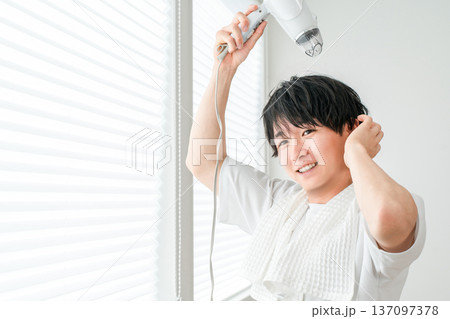 お風呂上がりにヘアドライヤーで髪を乾かす若いアジア人男性 お風呂上がりにヘアドライヤーで髪を乾かす若いアジア人男性 137097378