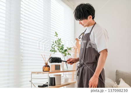 ほこり取り,ウールダスターで収納棚の埃を払うエプロン姿の男性 137098230