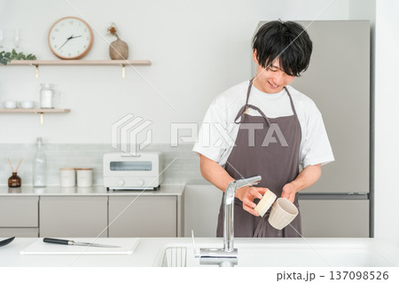 キッチンで洗い物をするエプロン姿の若いアジア人男性 137098526