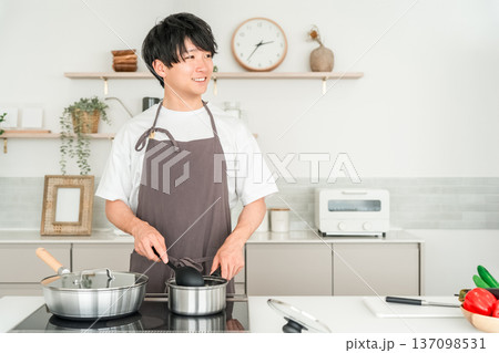 キッチンで料理をするエプロン姿の若いアジア人男性 キッチンで料理をするエプロン姿の若いアジア人男性 137098531