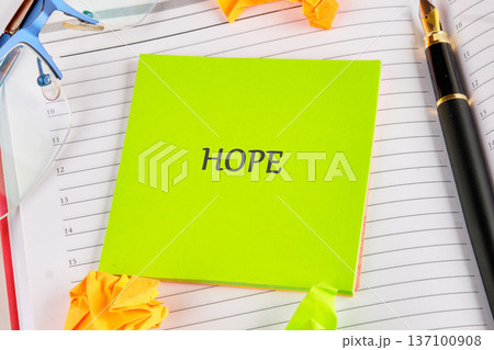 Green HOPE sticky note on a planner, surrounded by glasses a fountain pen, inviting positivity Green HOPE sticky note on a planner, surrounded by glasses a fountain pen, inviting positivity 137100908