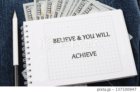 Believe achieve notebook page on dark denim with a white pencil and fanned 100 bills for prosperity Believe achieve notebook page on dark denim with a white pencil and fanned 100 bills for prosperity 137100947