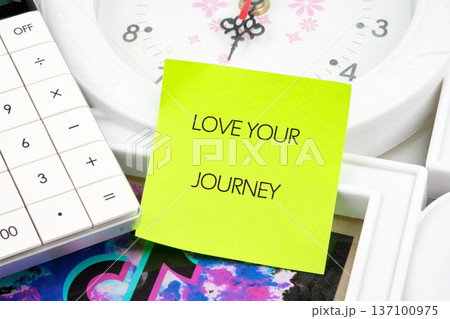 LOVE YOUR JOURNEY on a yellow sticky note, desk with calculator clock. A thoughtful daily affirmation LOVE YOUR JOURNEY on a yellow sticky note, desk with calculator clock. A thoughtful daily affirmation 137100975