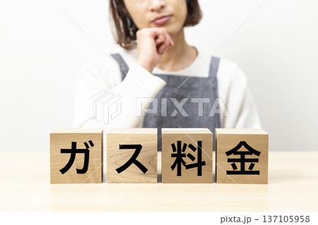 「ガス料金」と書かれたブロックとエプロン姿で悩む女性 「ガス料金」と書かれたブロックとエプロン姿で悩む女性 137105958