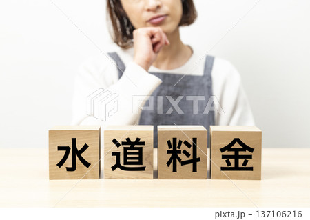 「水道料金」と書かれたブロックとエプロン姿で悩む女性 「水道料金」と書かれたブロックとエプロン姿で悩む女性 137106216