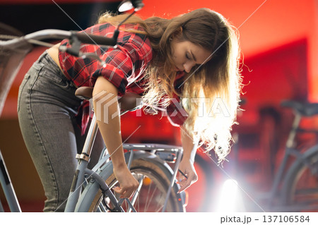 Young woman repairing bicycle wheel in workshop 137106584