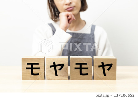 「モヤモヤ」と書かれたブロックとエプロン姿で悩む女性 137106652