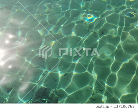 Sunlit clear water surface with green rippling reflections and light pattern for abstract background and texture design Sunlit clear water surface with green rippling reflections and light pattern for abstract background and texture design 137106765