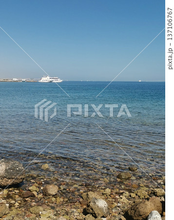 Calm coastal shoreline with clear shallow water and distant white ferry for travel banner and seaside background design Calm coastal shoreline with clear shallow water and distant white ferry for travel banner and seaside background design 137106767