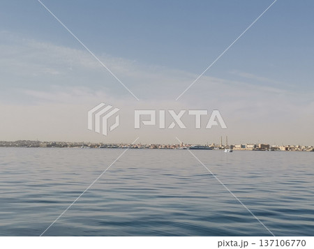 Wide tranquil bay with gentle ripples and distant coastal town skyline for calm seascape background and landscape design 137106770