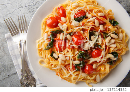 Fettuccine pasta with white beans, cherry tomatoes and spinach close-up in a plate. Horizontal top view Fettuccine pasta with white beans, cherry tomatoes and spinach close-up in a plate. Horizontal top view 137114582