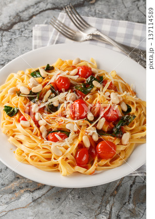 Italian tagliatelle pasta served on a white plate with roasted cherry tomatoes, white beans, spinach and grated parmesan closeup on the plate. Vertical 137114589