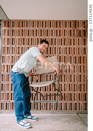 Man adjusting portable chair against unique textured brick wall Man adjusting portable chair against unique textured brick wall 137114830