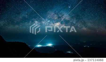 Panoramic view of the Milky Way galaxy over a mountain ridge with glowing city lights in the valley. Panoramic view of the Milky Way galaxy over a mountain ridge with glowing city lights in the valley. 137114860
