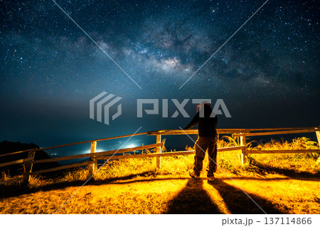 Silhouette of a person standing by a wooden fence admiring the majestic starry night sky and Milky Way. Silhouette of a person standing by a wooden fence admiring the majestic starry night sky and Milky Way. 137114866