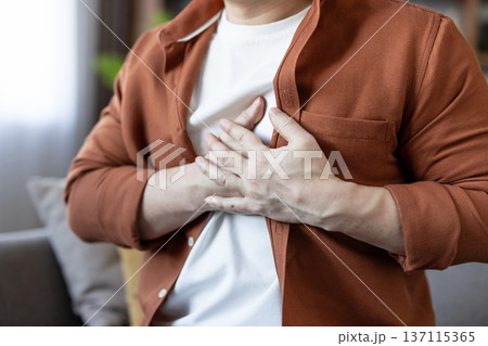 Middle-aged man clutching his chest with both hands, sudden severe chest pain and distress suggesting heart attack or acute cardiac emergency at home or in public 137115365