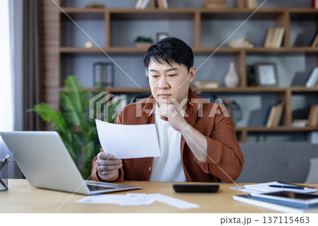 Man checking bills and preparing taxes at his home office, analyzing financial documents and using a laptop and calculator for budgeting and debt management 137115463