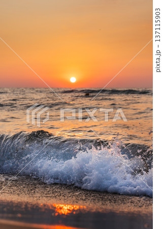 Sea wave splashing on sandy beach during colorful sunset over horizon with warm orange sky Sea wave splashing on sandy beach during colorful sunset over horizon with warm orange sky 137115903