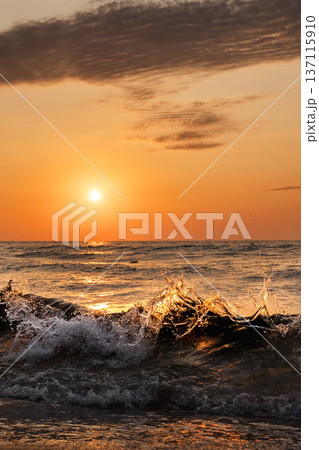 Ocean wave splashing at sunset with golden sunlight reflection on water and dramatic sky background Ocean wave splashing at sunset with golden sunlight reflection on water and dramatic sky background 137115910