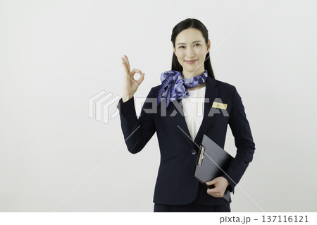 白背景の紺のスーツにリボン、ネームタグをつけて指で丸のokのポーズをする笑顔の日本人女性　コンシェル 137116121