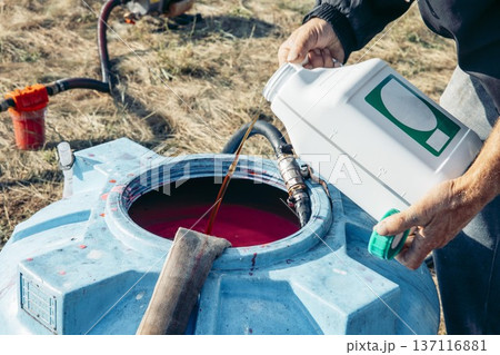 men's hands pouring a chemical into a large blue plastic tank filled, agricultural mixing process, hoses connected for chemical transfer in sunny rural field, agriculture, irrigation, chemistry men's hands pouring a chemical into a large blue plastic tank filled, agricultural mixing process, hoses connected for chemical transfer in sunny rural field, agriculture, irrigation, chemistry 137116881