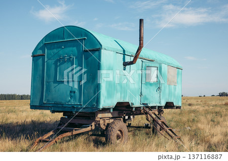 A vintage turquoise agricultural trailer stands in a grassy field under a clear blue sky. The trailer is weathered and shows signs of use in farming activities. 137116887