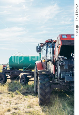 red agricultural tractor parked on rural field with water tank trailer blue sky open countryside landscape with large copy space banner composition concept of agriculture, farming equipment, vertical red agricultural tractor parked on rural field with water tank trailer blue sky open countryside landscape with large copy space banner composition concept of agriculture, farming equipment, vertical 137116892