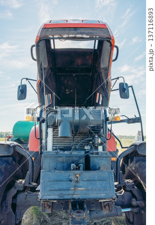 red agricultural tractor parked on rural field, water tank trailer under blue sky open countryside landscape, concept of agriculture, farming equipment 137116893