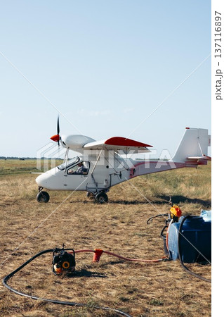 Small agricultural airplane on a farm field. The aircraft is equipped for spraying chemicals. Nearby equipment includes a tank and hoses. Small agricultural airplane on a farm field. The aircraft is equipped for spraying chemicals. Nearby equipment includes a tank and hoses. 137116897
